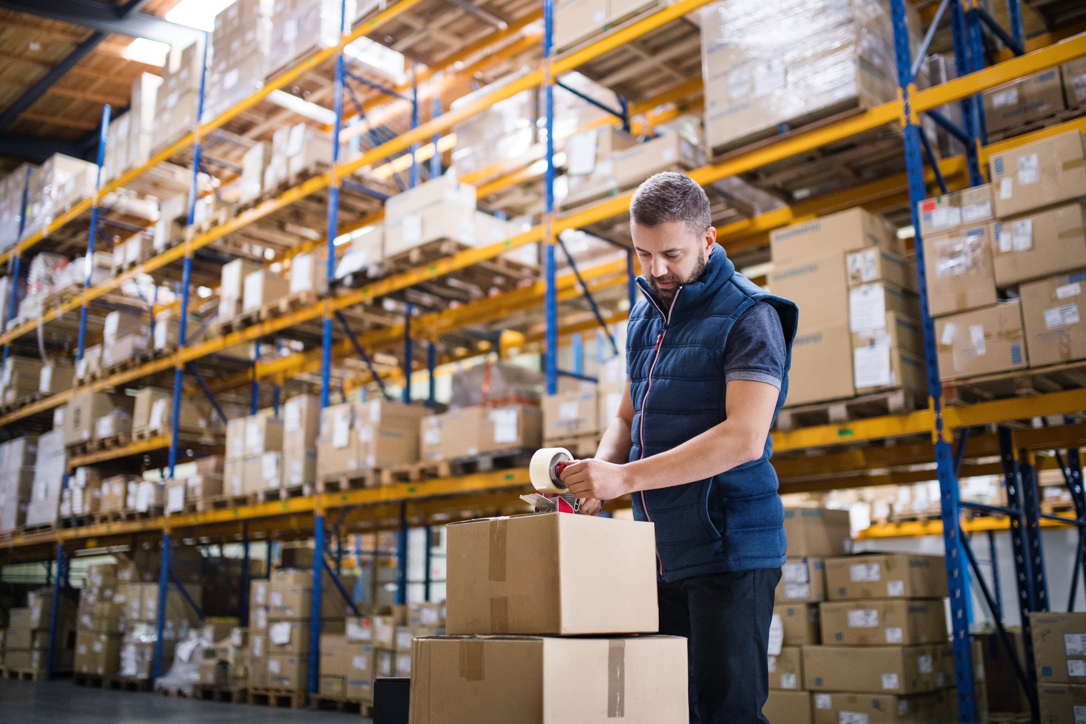 Male Warehouse Worker Sealing Cardboard Boxes